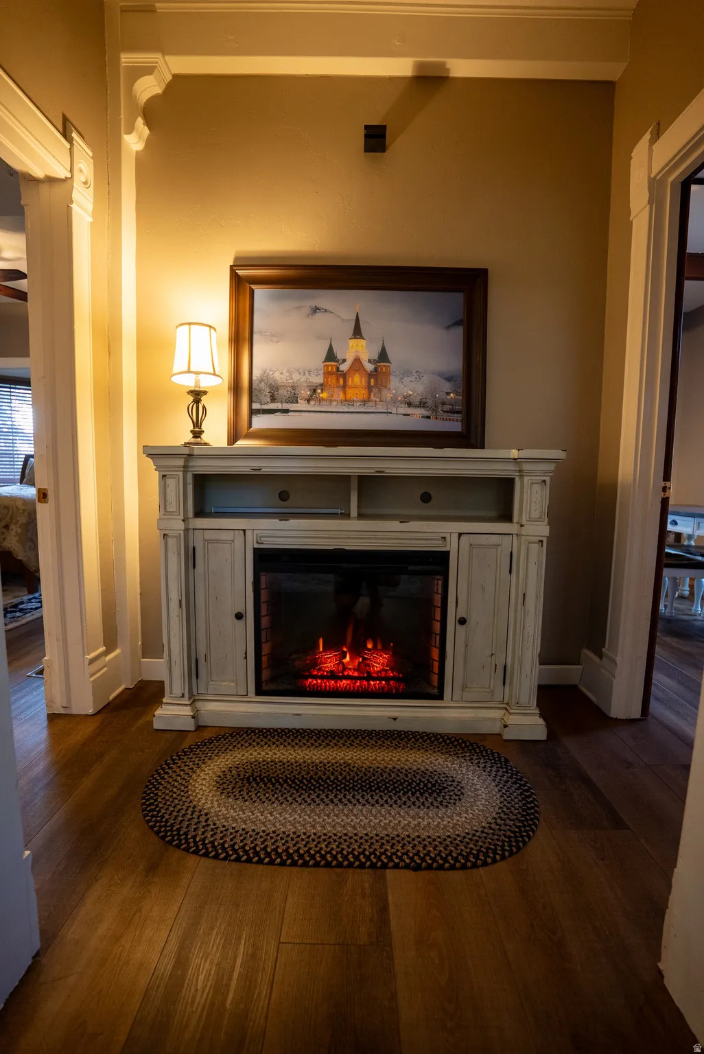 Decorative fireplace console with an electric insert, wood-finish flooring, substantial crown molding, and ornate door casings