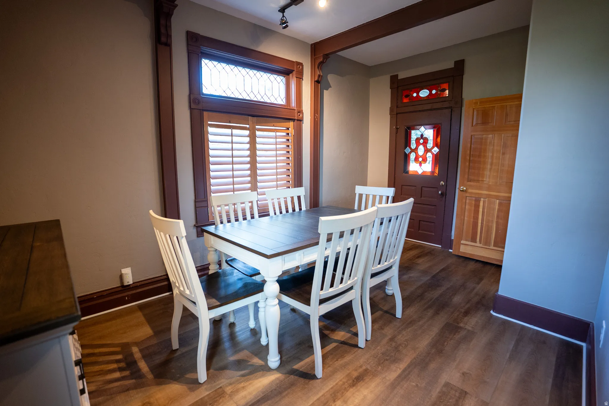 Dining area featuring dark wood-finish flooring, a decorative transom window with wood shutters, and a stained glass entry door