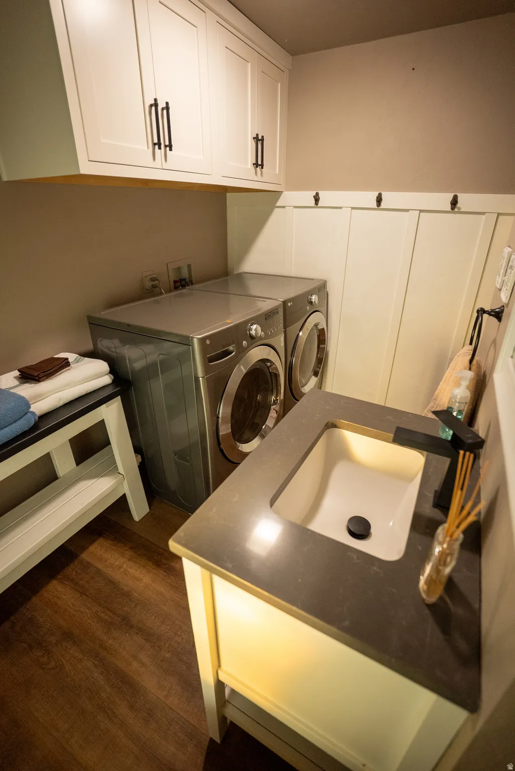 Laundry area featuring wood-finish flooring, white shaker cabinetry with dark hardware, and a board and batten wall treatment