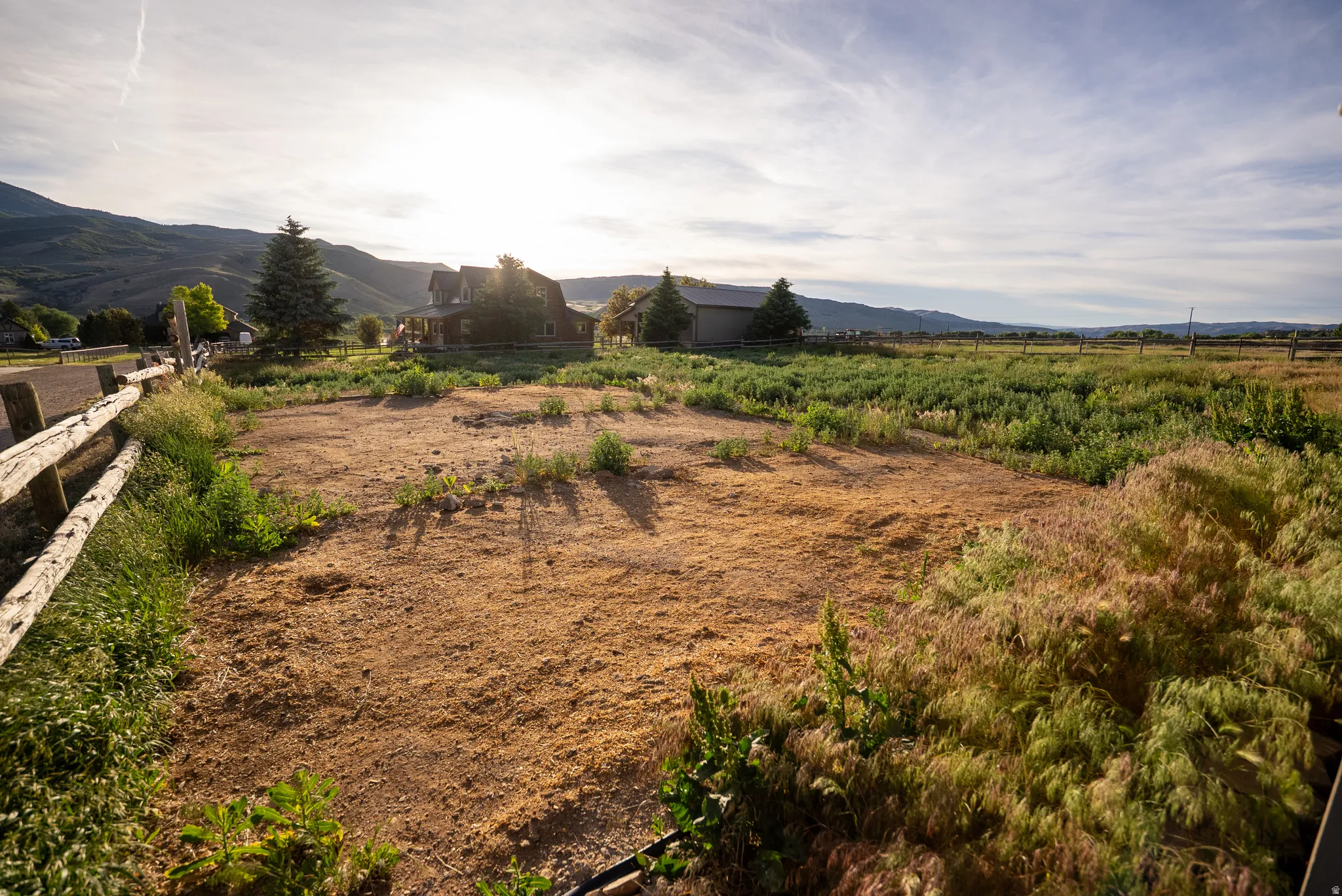 Expansive land parcel featuring open terrain, a rustic wooden fence, mountainous backdrop, and distant structures