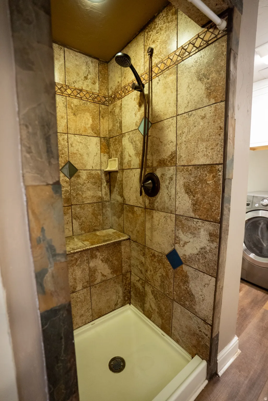 Shower stall featuring stone-look tile walls with decorative accent tiles, a built-in bench, and a hand-held shower fixture
