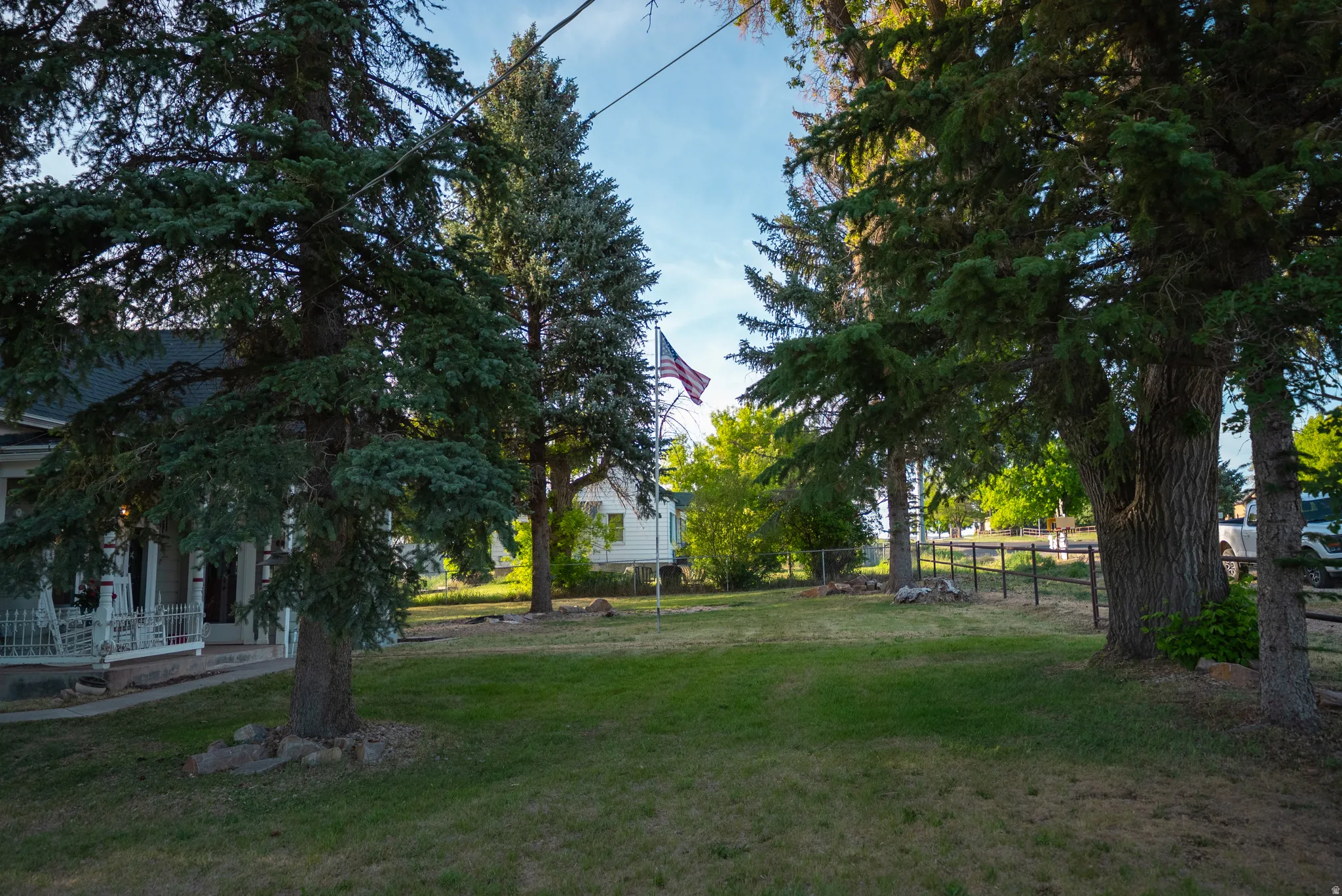 Expansive lawn bordered by mature trees and a partial metal fence