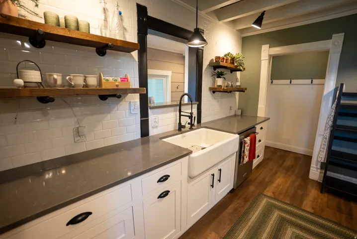 Kitchenette featuring a farmhouse sink, dark stone-finish countertops, subway tile backsplash, and wood-finish flooring