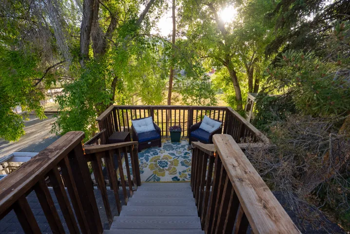 Elevated wood-finish deck with full railing and steps, surrounded by mature trees