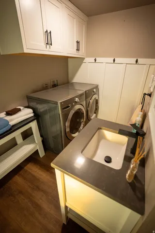 Laundry area featuring wood-finish flooring, white shaker cabinetry with dark hardware, and a board and batten wall treatment