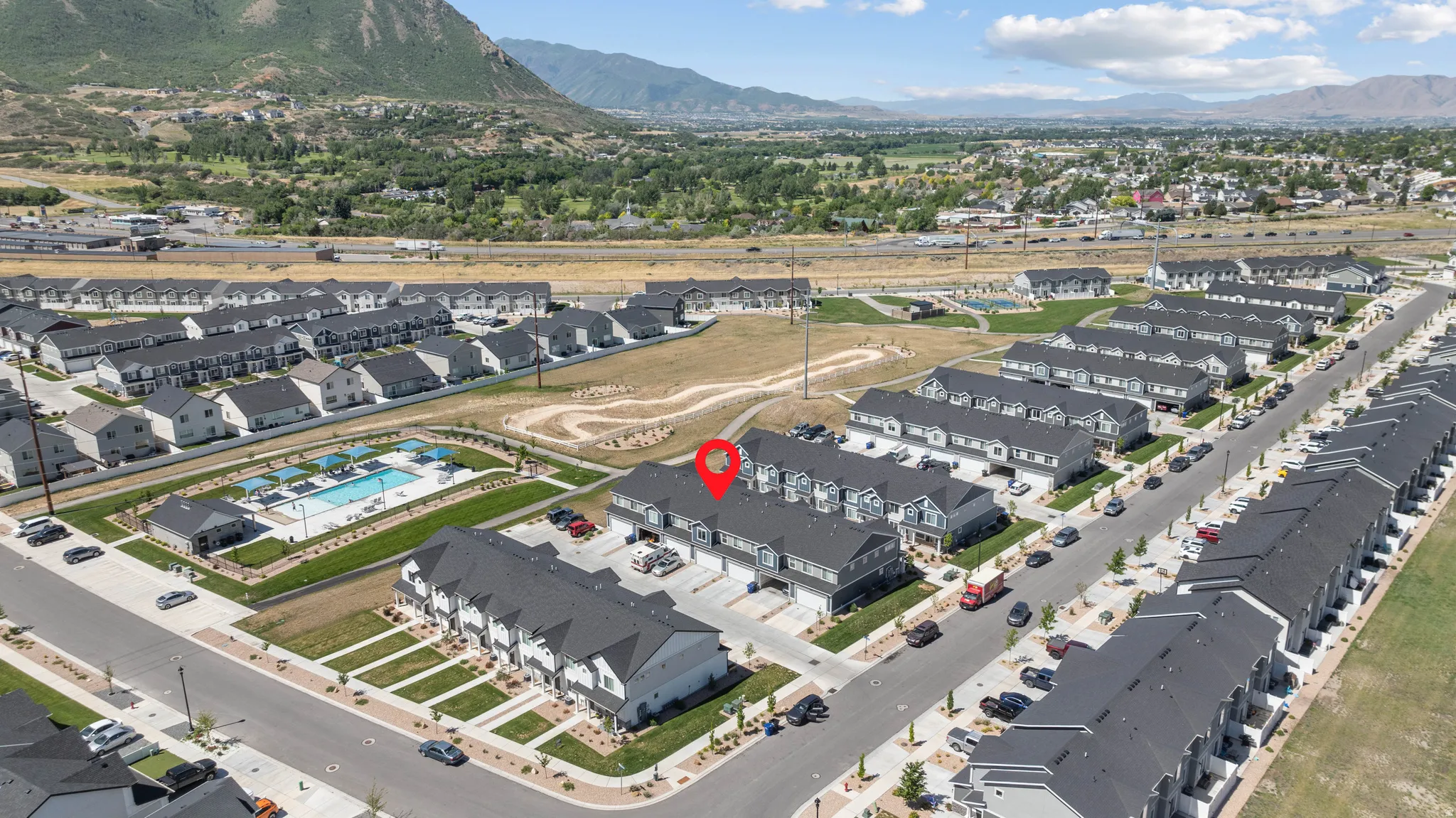 Aerial view of a residential community featuring multiple rows of townhomes with dark gray roofs and light-colored siding