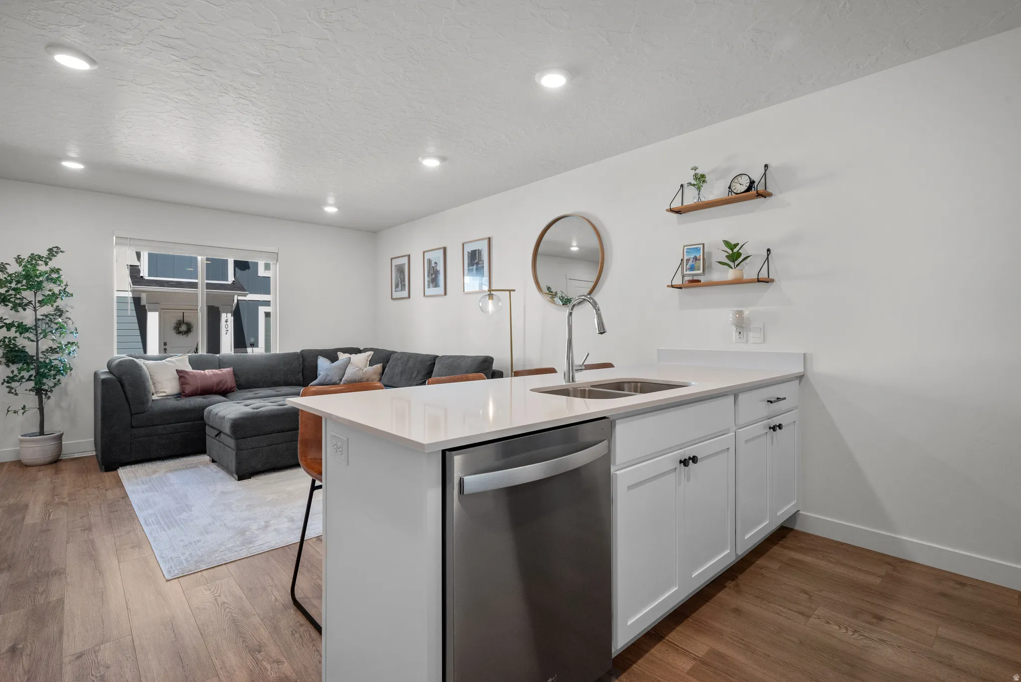 Open-concept living area featuring wood-finish flooring, recessed lighting, and a kitchen island with a stainless steel sink and dishwasher