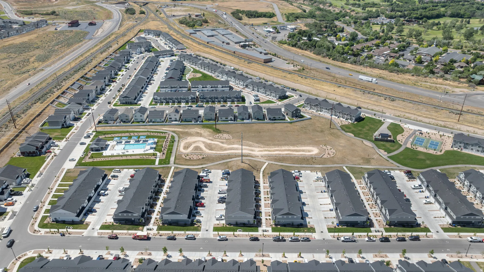 Community layout featuring multiple residential buildings with dedicated parking, a central swimming pool with surrounding lounge areas, and recreational courts