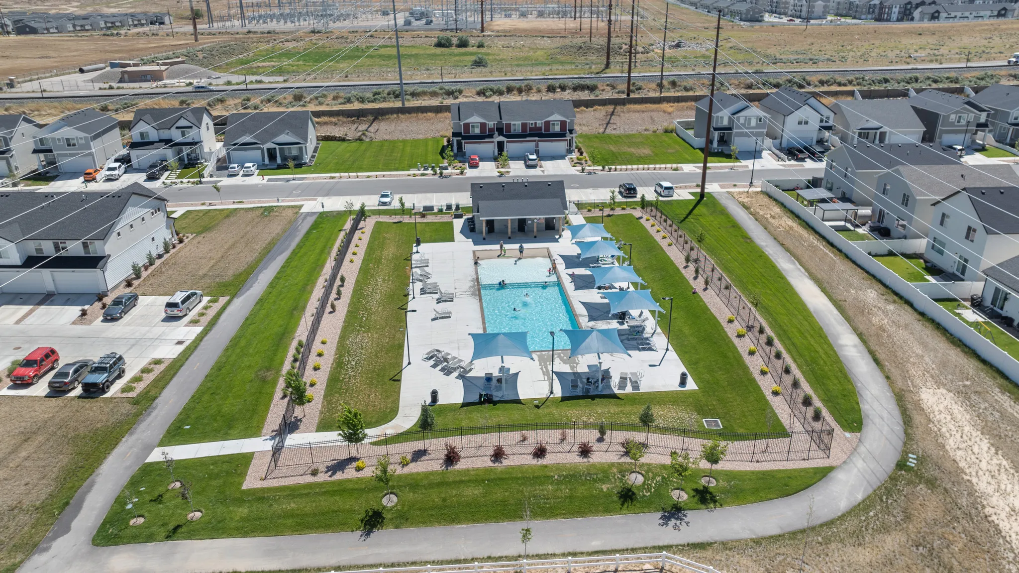 Community pool area featuring a rectangular swimming pool, surrounding lounge seating, and multiple shade structures