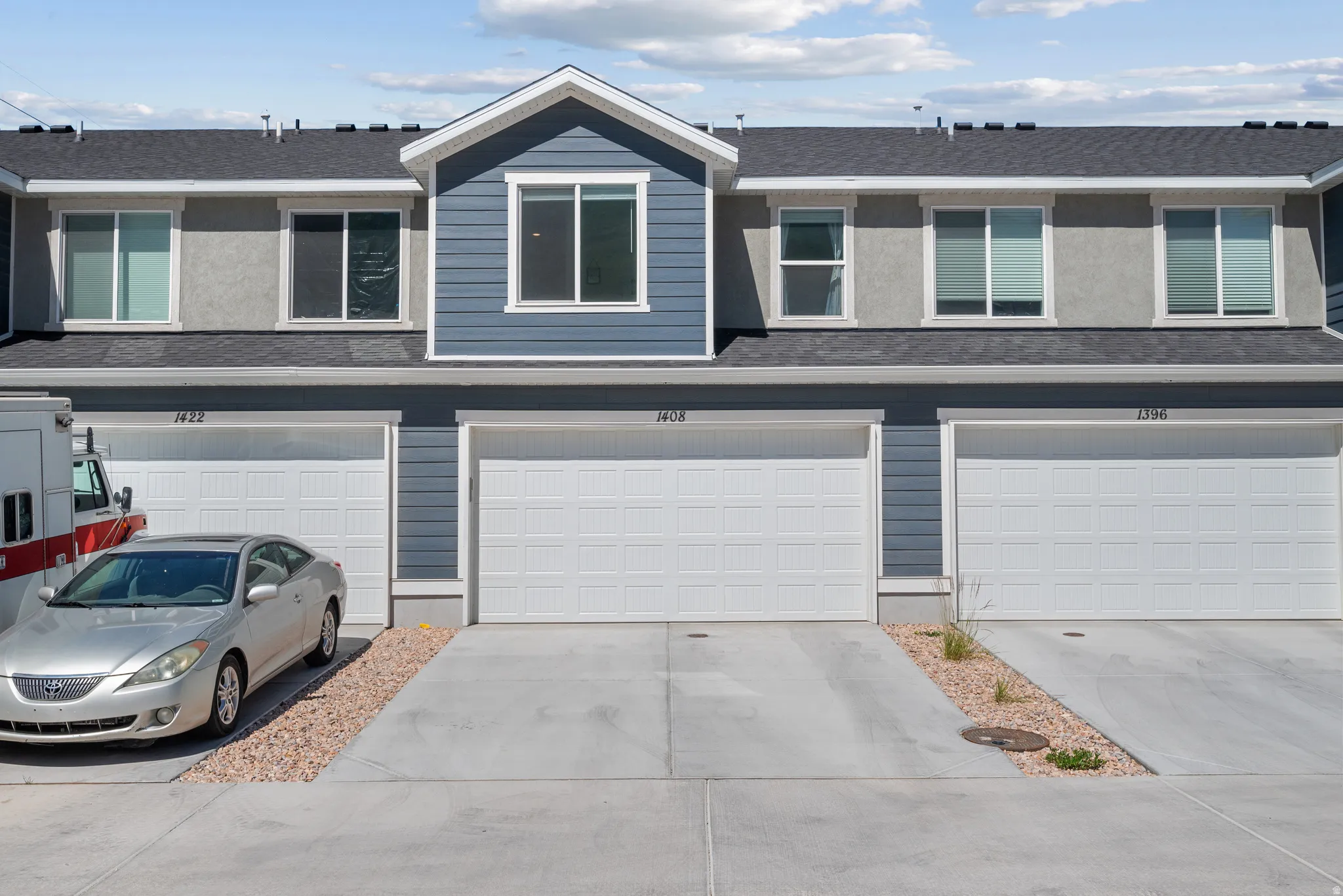 Modern townhome exterior featuring a prominent gabled entry, gray horizontal siding, and multiple white-framed windows