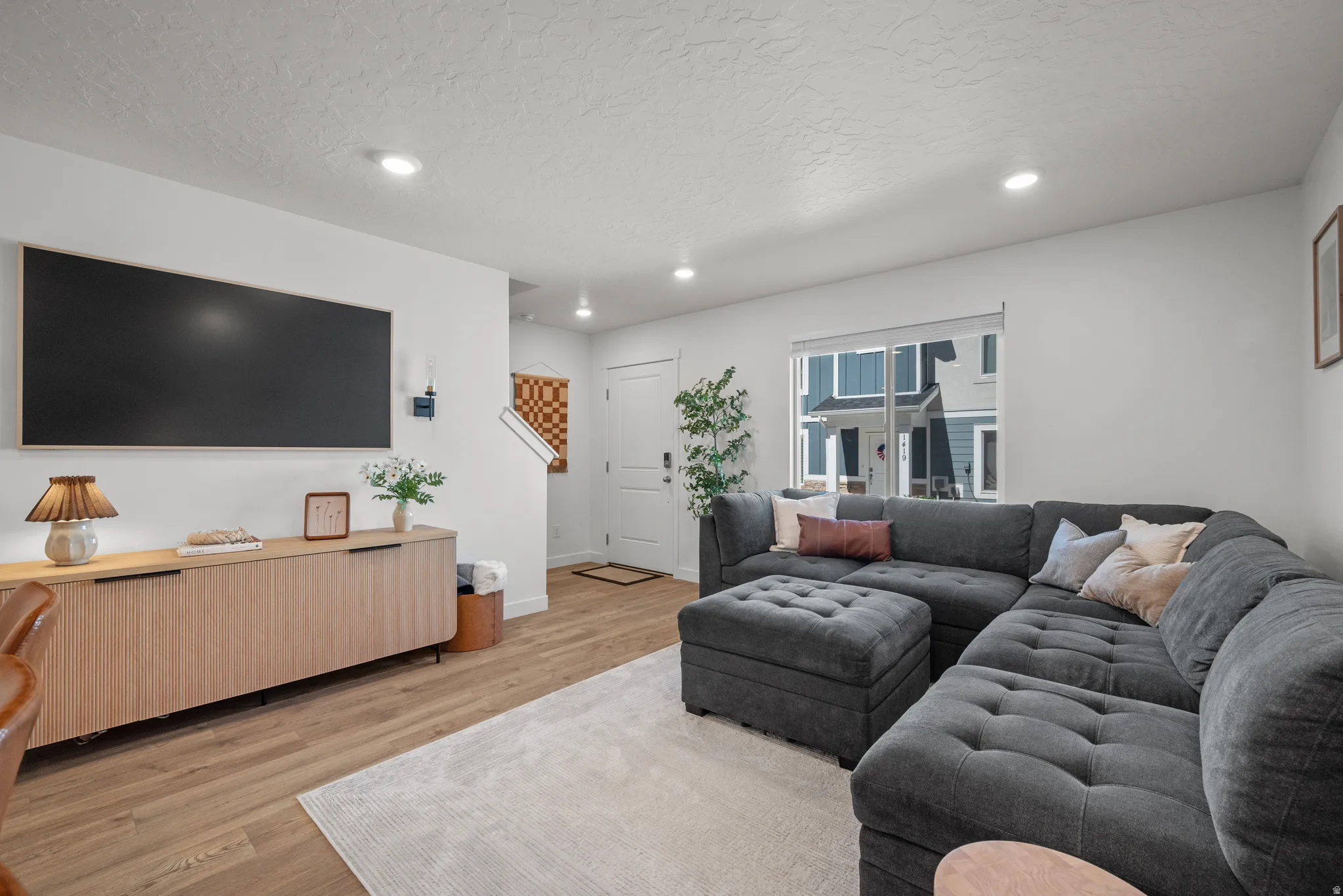 Spacious living area featuring wood-finish flooring, recessed lighting, and a front entry door with a multi-pane window