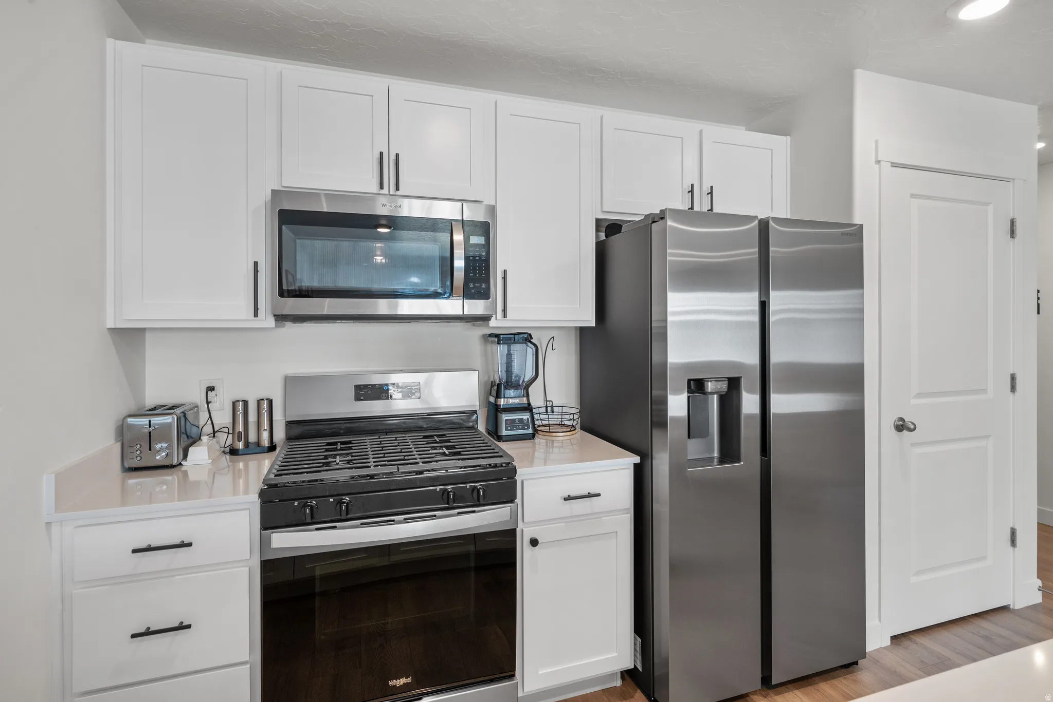 Kitchen featuring white shaker cabinetry, stainless steel appliances, a gas range with an oven, an over-the-range microwave, and light-toned countertops