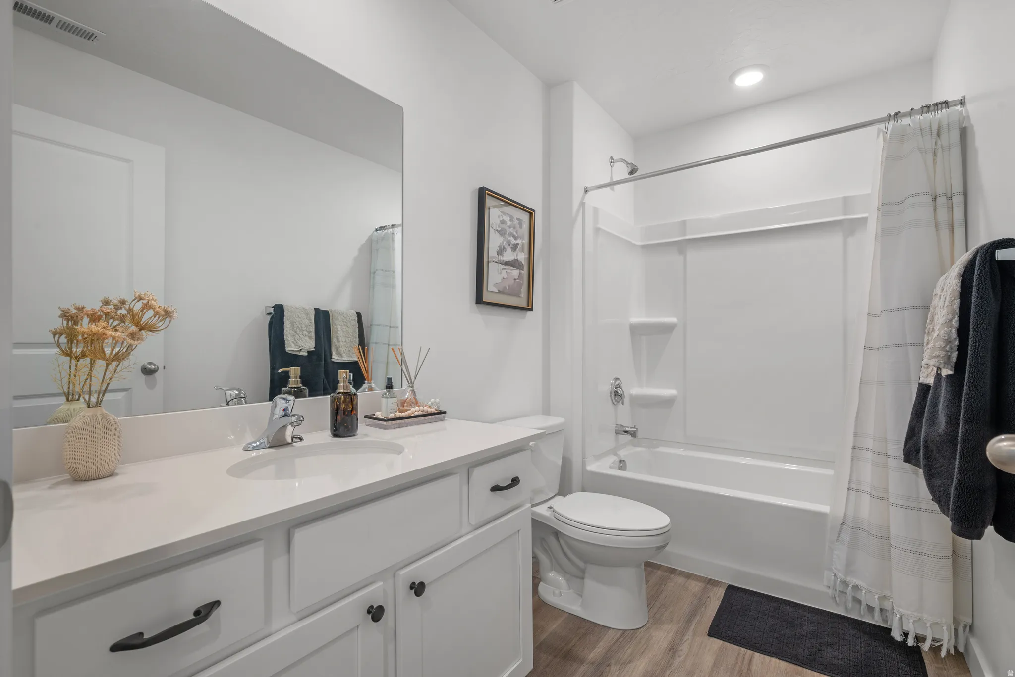 Bathroom featuring a single vanity with a white countertop, wood-finish flooring, recessed lighting, and a bathtub with a shower