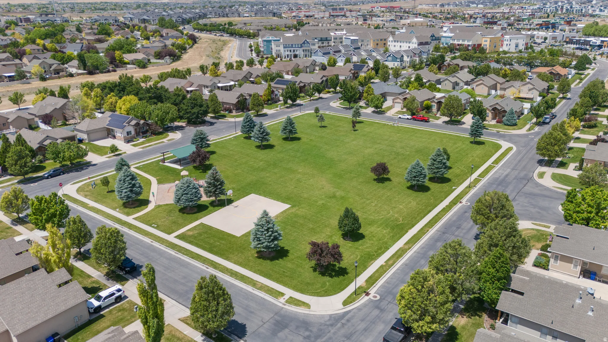 Central green space featuring a manicured lawn, established trees, and paved perimeter pathways