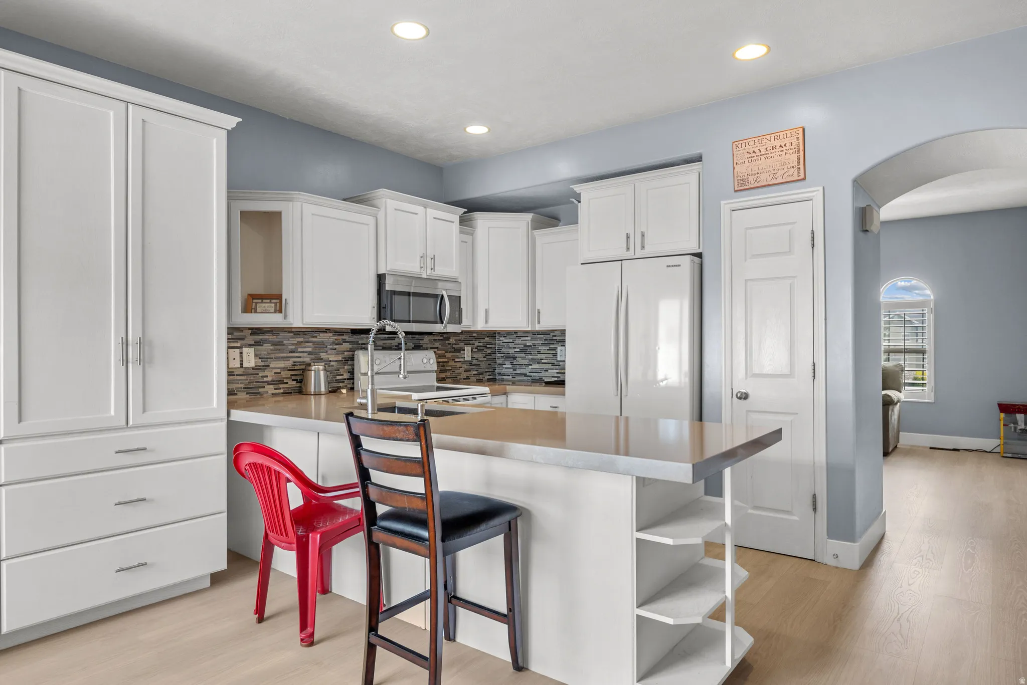 Kitchen featuring white cabinetry, a central island with integrated shelving, light wood-finish flooring, recessed lighting, and an arched doorway