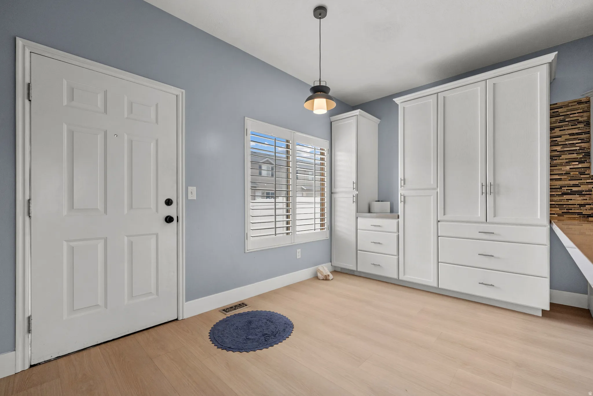 Entryway featuring wood-finish flooring, white paneled door, and extensive built-in white cabinetry with chrome hardware