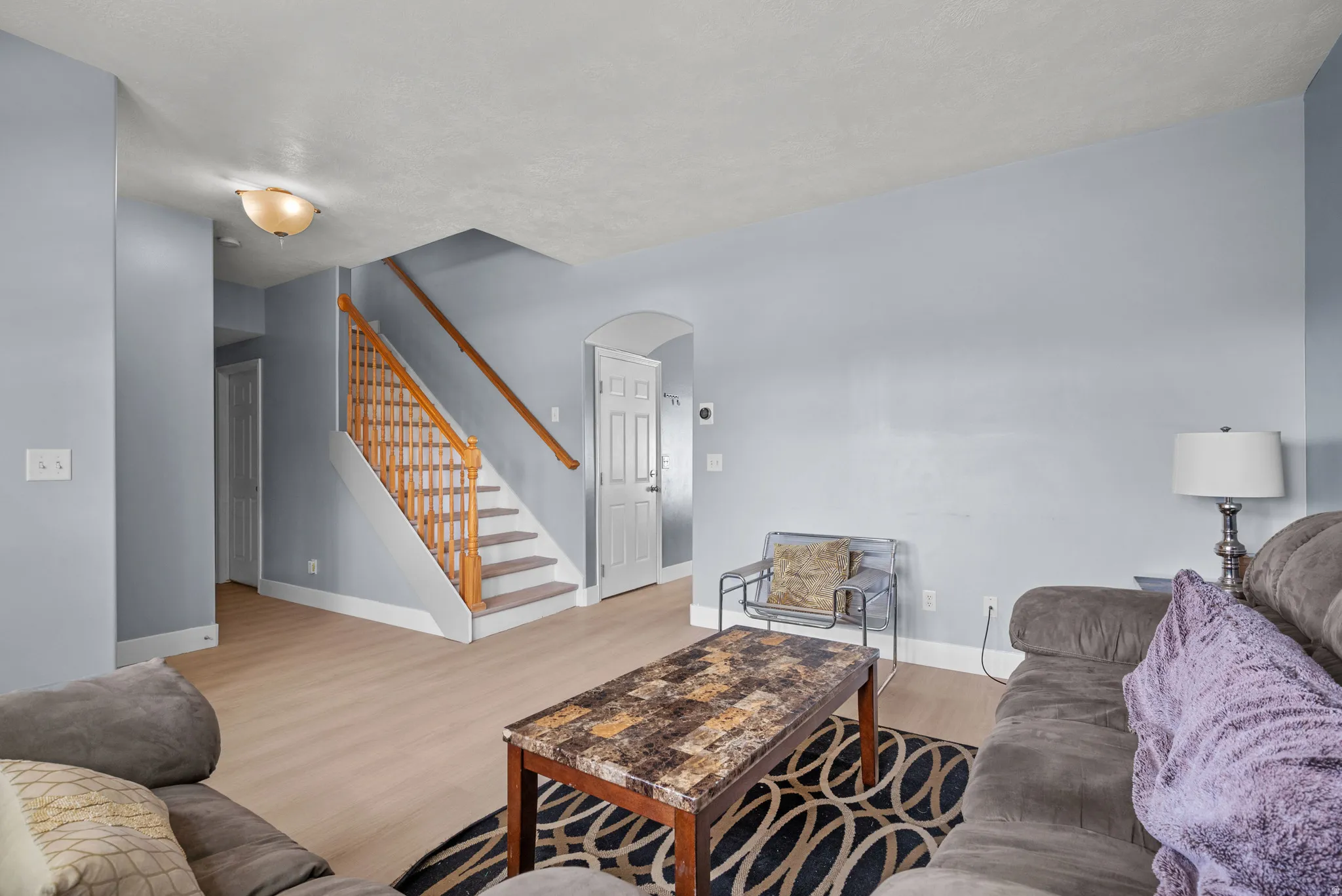 Spacious living area featuring light wood-finish flooring and a staircase with natural wood railings