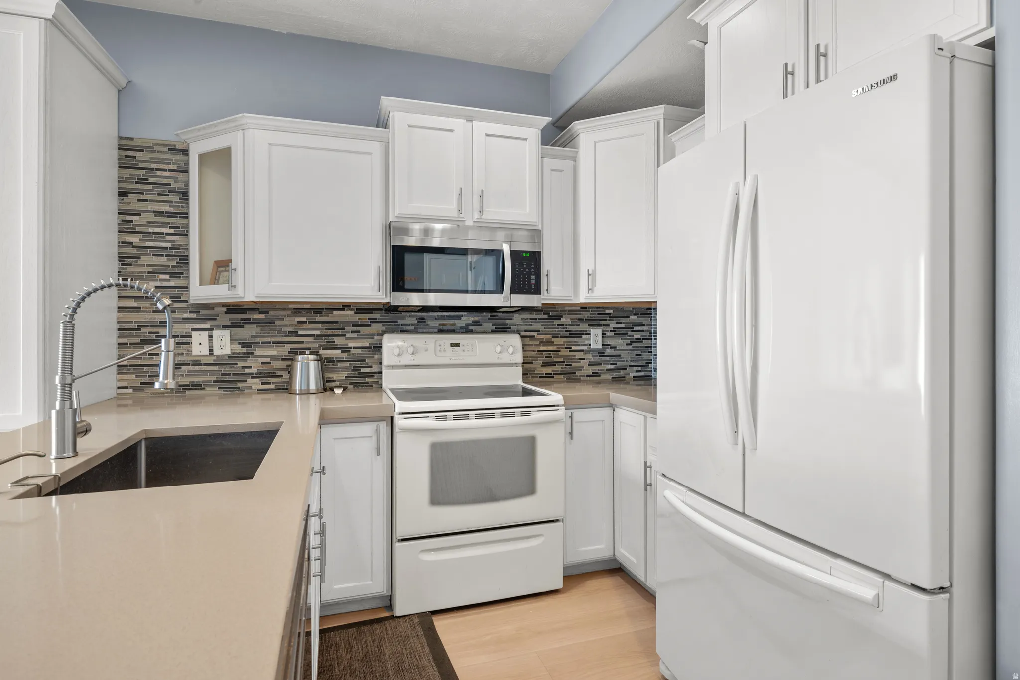 Kitchen featuring white cabinetry, a mosaic tile backsplash, and light-toned countertops