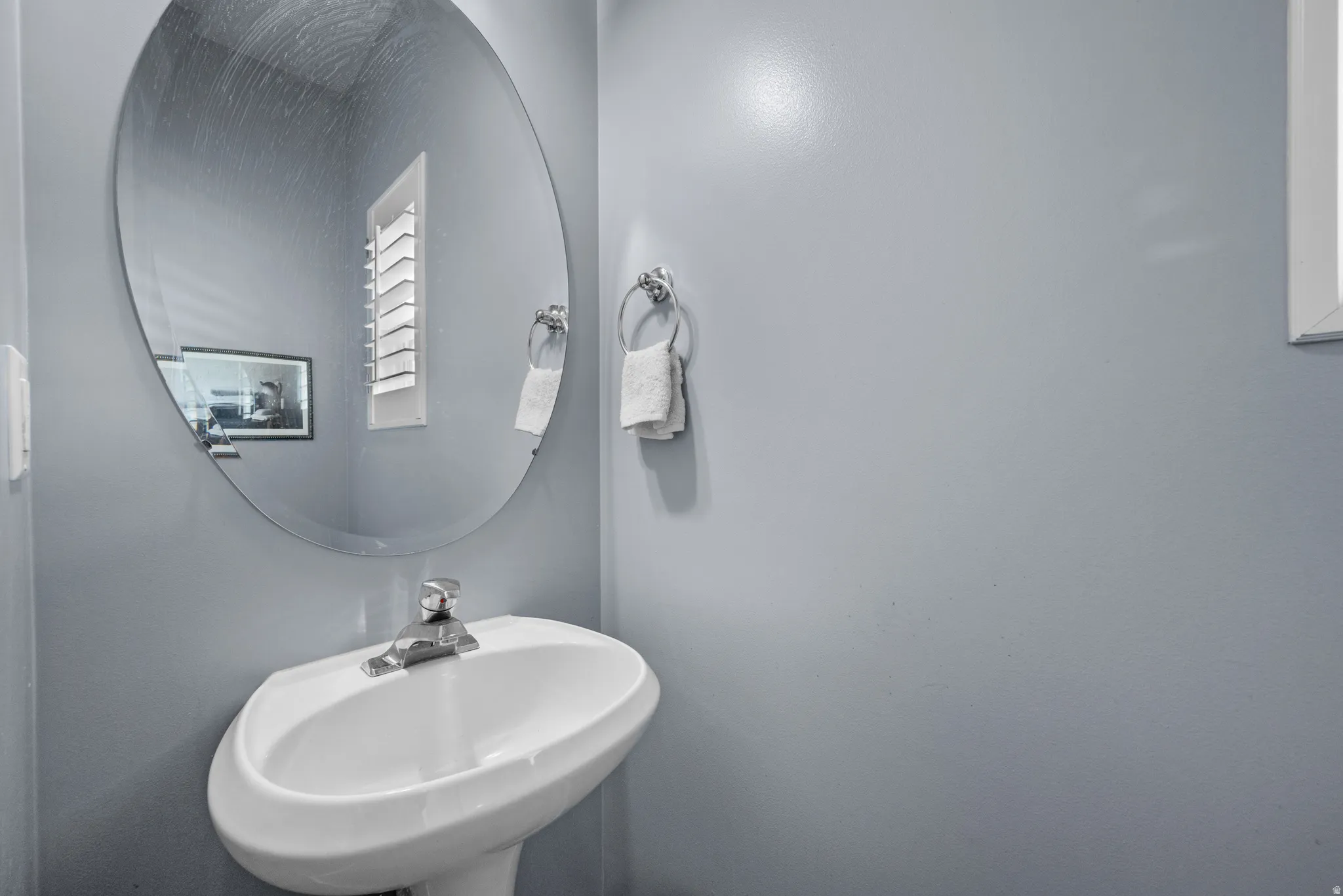 Pedestal sink with chrome faucet, complemented by a large oval mirror