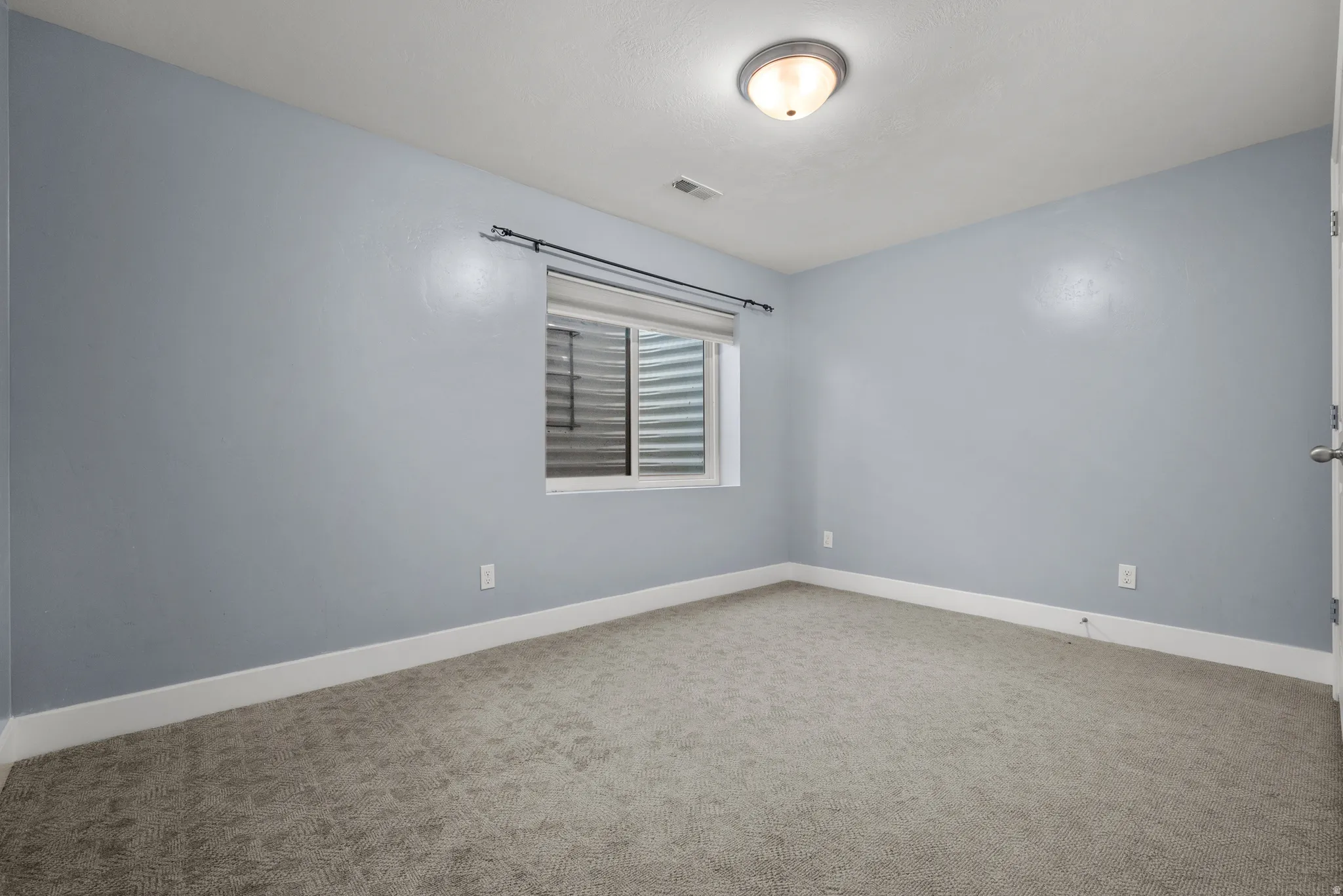 Carpeted room with a window featuring horizontal blinds, light blue walls, white baseboards, and a semi-flush mount ceiling light