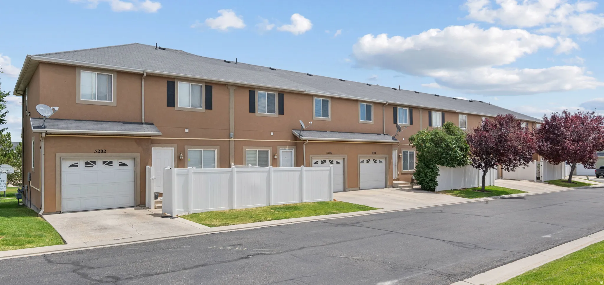Multi-unit dwelling featuring individual attached garages, a two-story stucco exterior, and a white picket fence