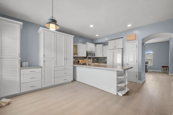 White cabinetry with extensive storage, light wood-finish flooring, recessed lighting, and a kitchen island with built-in shelving