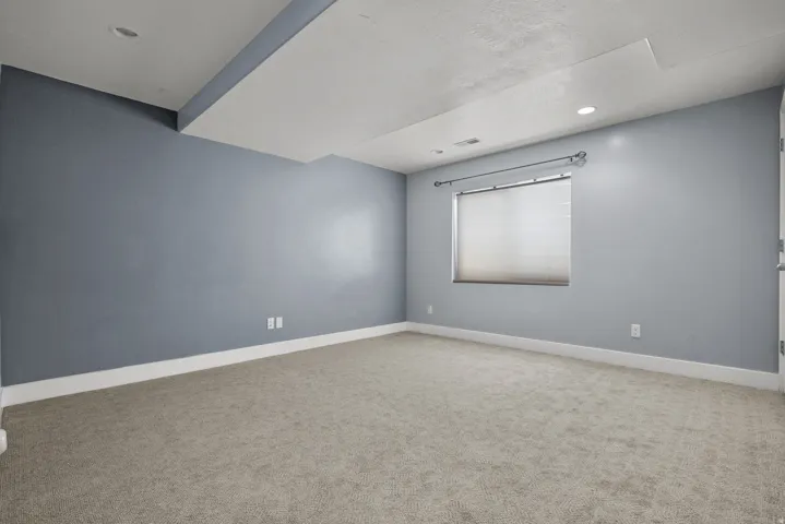 Spacious interior room featuring light gray carpeting, recessed ceiling lighting, and a window with blinds