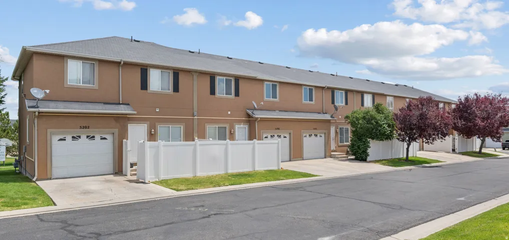 Multi-unit dwelling featuring individual attached garages, a two-story stucco exterior, and a white picket fence