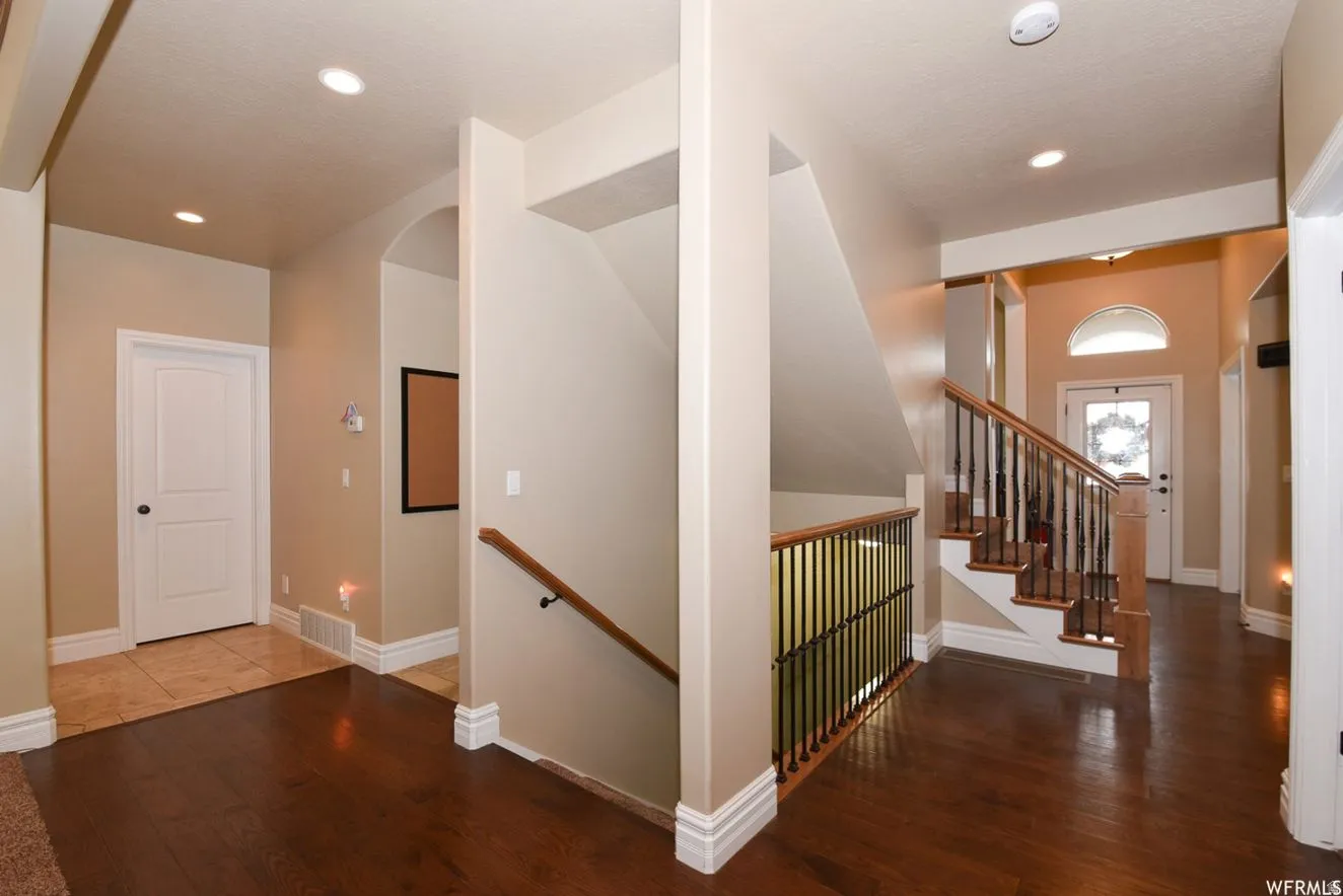 Foyer showcasing a wood-finish flooring, a staircase with wood handrails and wrought iron balusters, recessed lighting, and an arched entry with a transom window