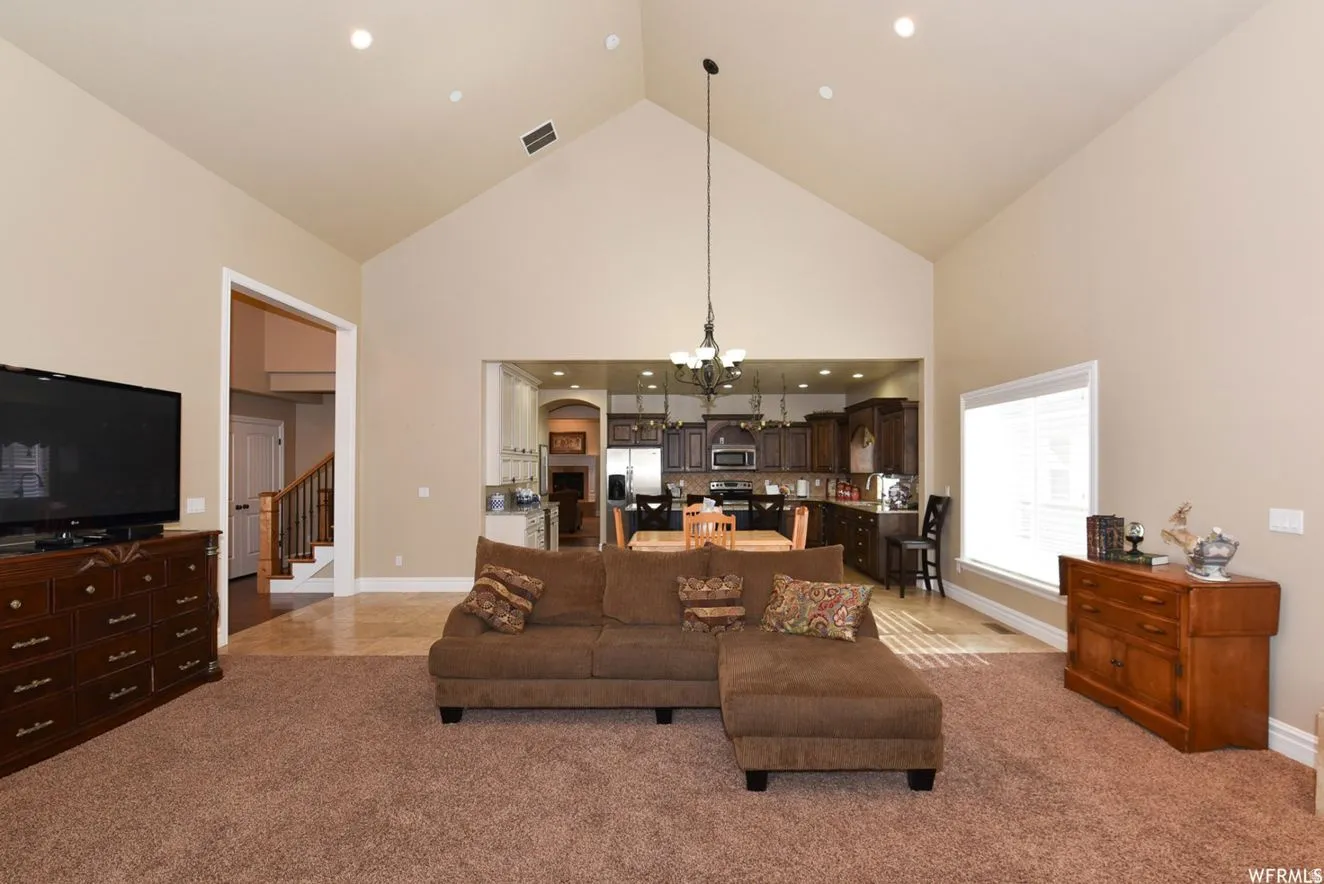 Vaulted ceiling great room featuring recessed lighting, a large window with blinds, and an open concept layout into the kitchen and dining areas