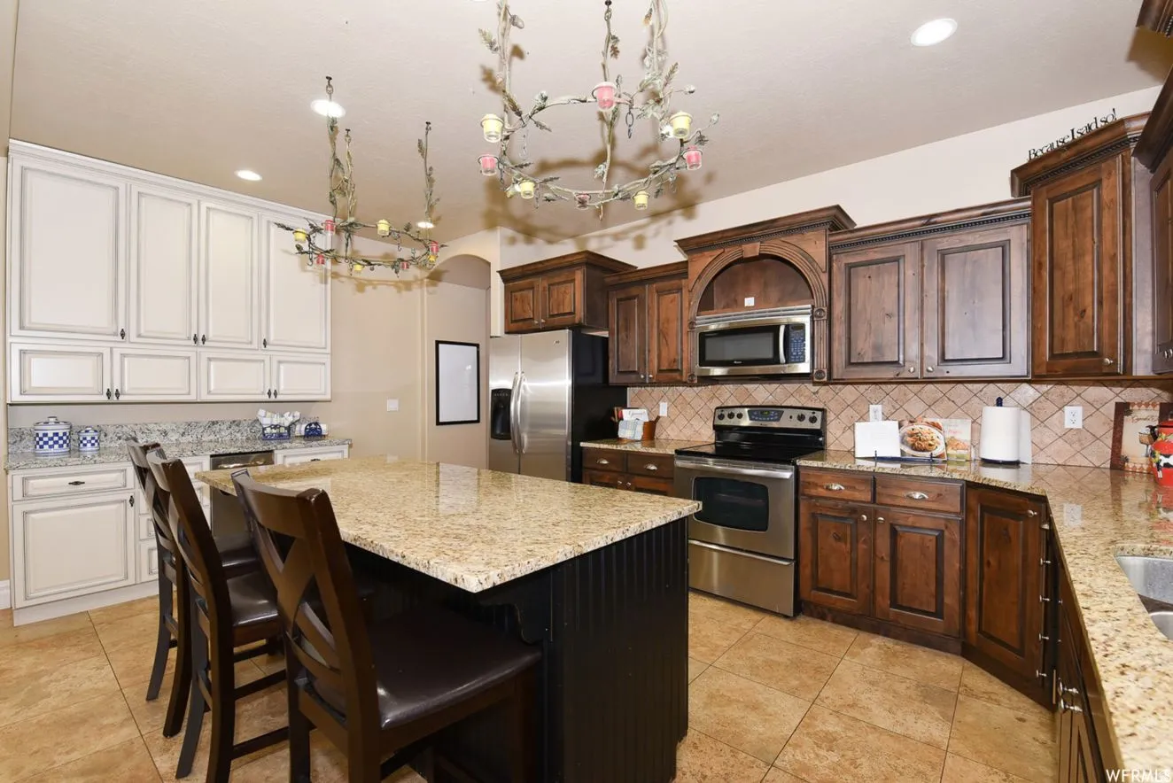 Spacious kitchen featuring an expansive granite island, integrated stainless-steel appliances, and a blend of rich wood and white cabinetry