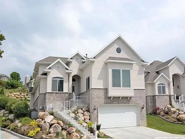 Contemporary stucco and stone-faced residence featuring a two-car garage, multiple gabled rooflines, and a prominent front entry with a stairway