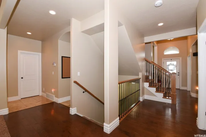 Foyer showcasing a wood-finish flooring, a staircase with wood handrails and wrought iron balusters, recessed lighting, and an arched entry with a transom window