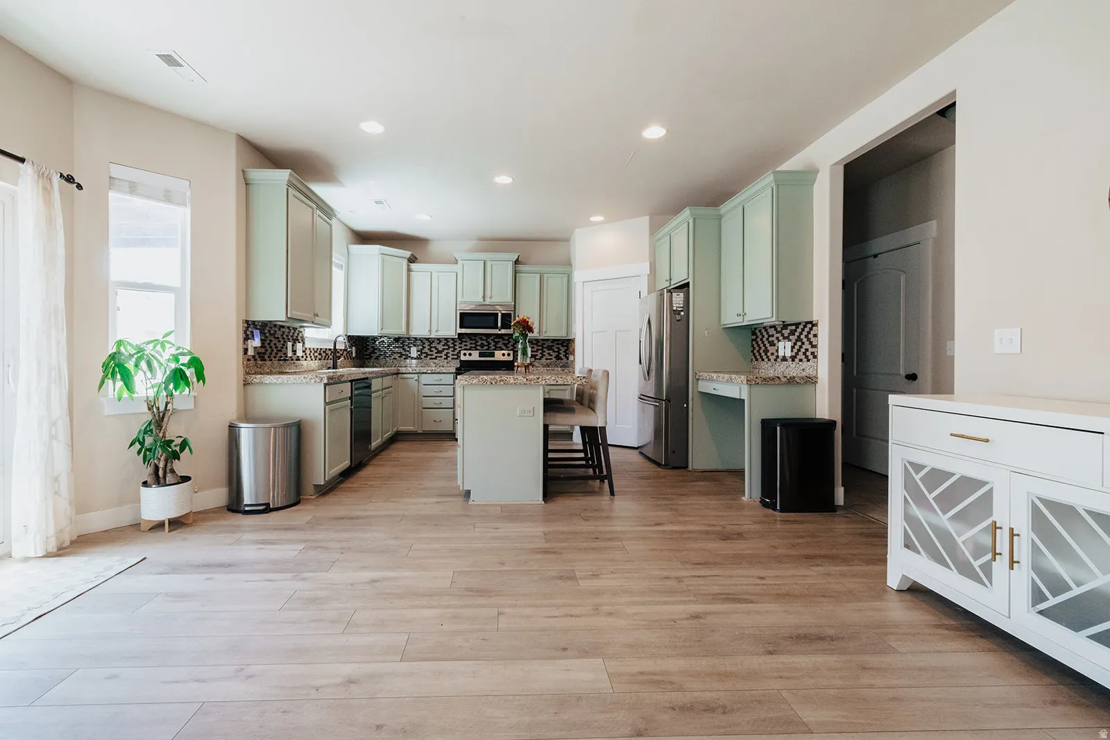 Open-concept kitchen featuring light-toned cabinetry, stainless steel appliances, a center island, and wood-finish flooring