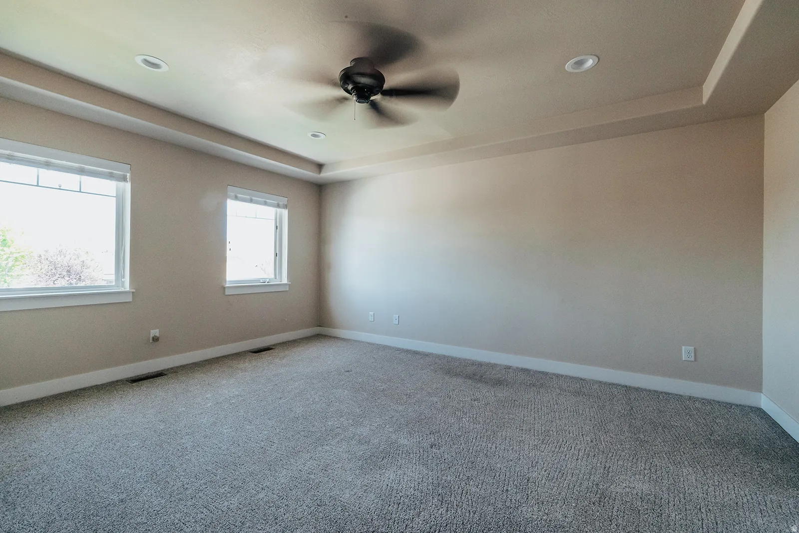 Spacious room with tray ceiling, recessed lighting, ceiling fan, and light-toned carpeting