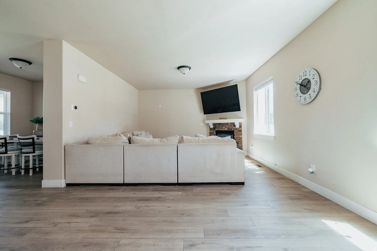 Open-concept living space featuring wood-finish flooring, a stone fireplace with a white mantel, and a bright window