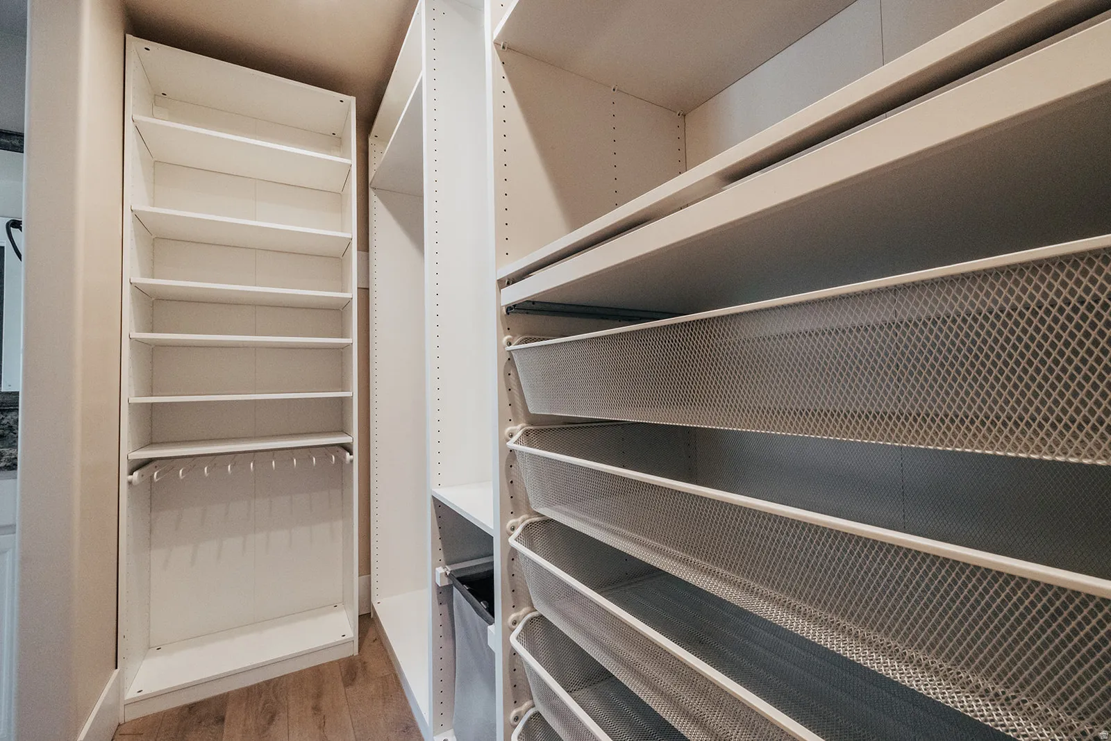 Custom closet system featuring white shelving units, multiple wire mesh pull-out drawers, and integrated hanging storage