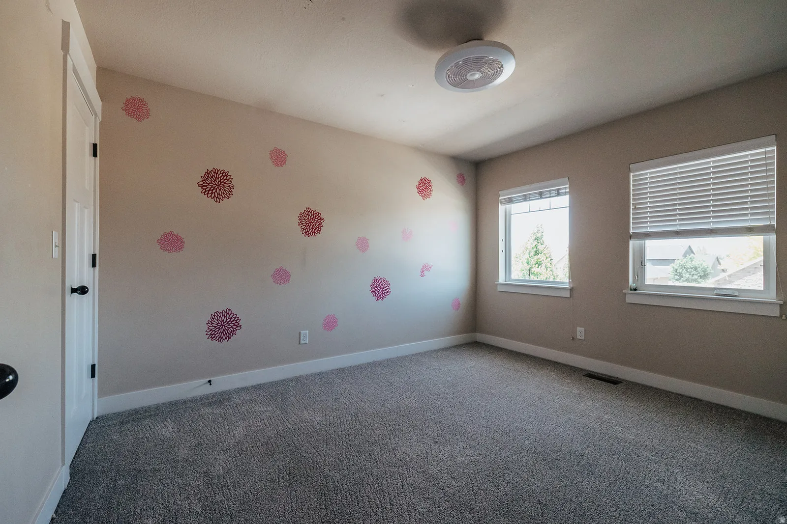 Carpeted interior room with two windows, a white door, and a ceiling-mounted light fixture