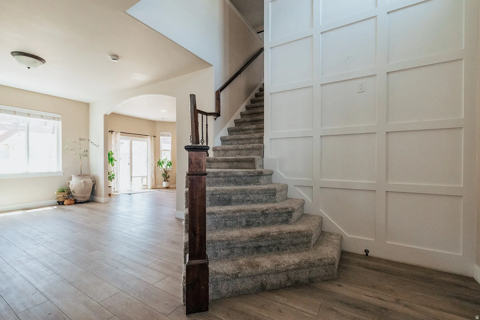 Carpeted staircase with dark wood-finish newel post and handrail, complemented by a wainscoted wall