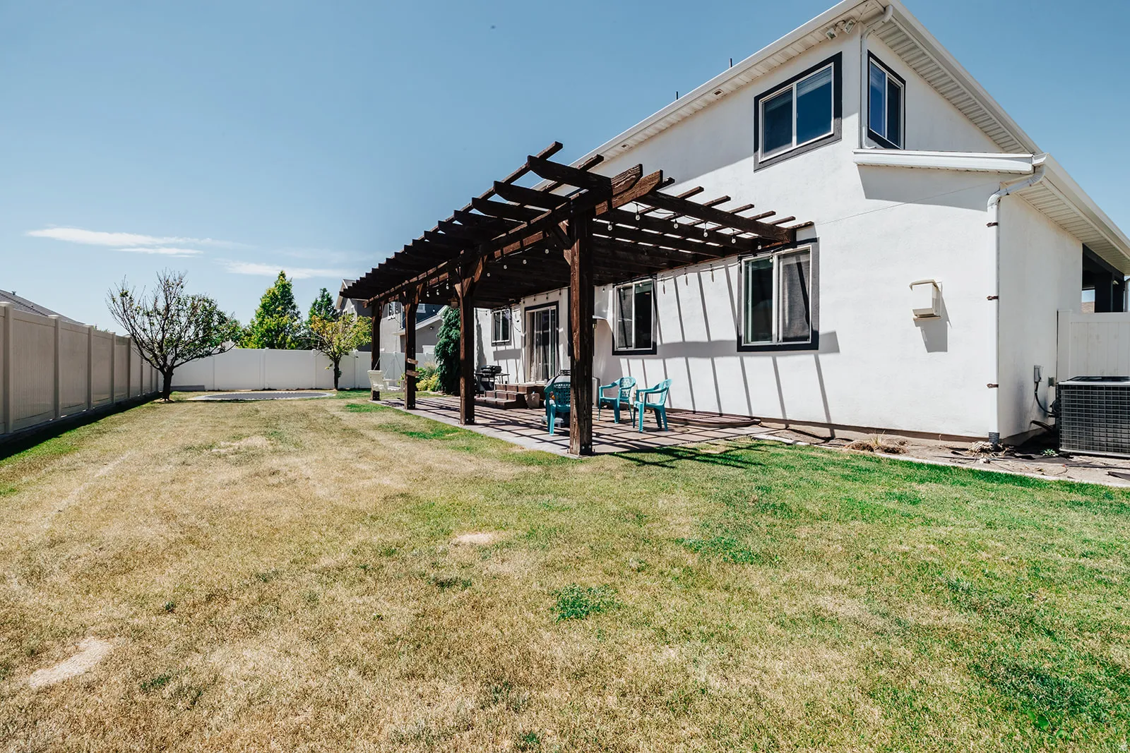 Expansive backyard featuring a pergola-covered patio, mature trees, a privacy fence, and a stucco exterior with multiple windows