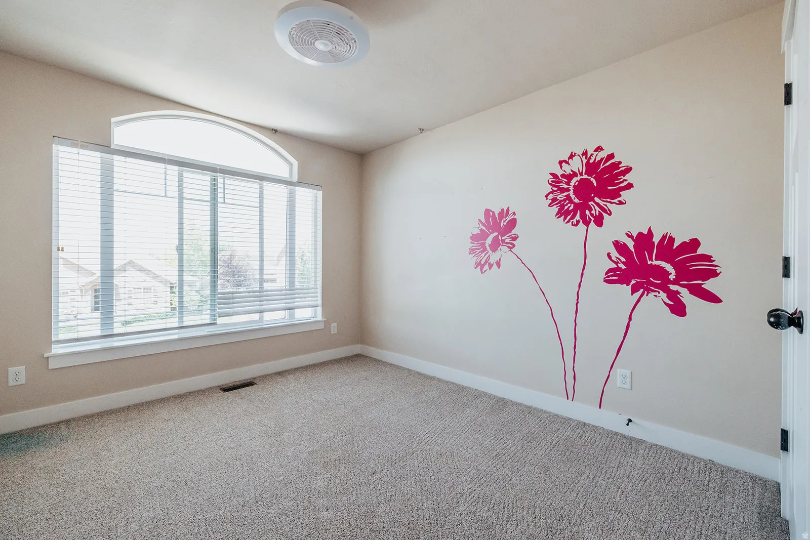 Room featuring a large window with an arched transom, beige carpeting, and a ceiling fan
