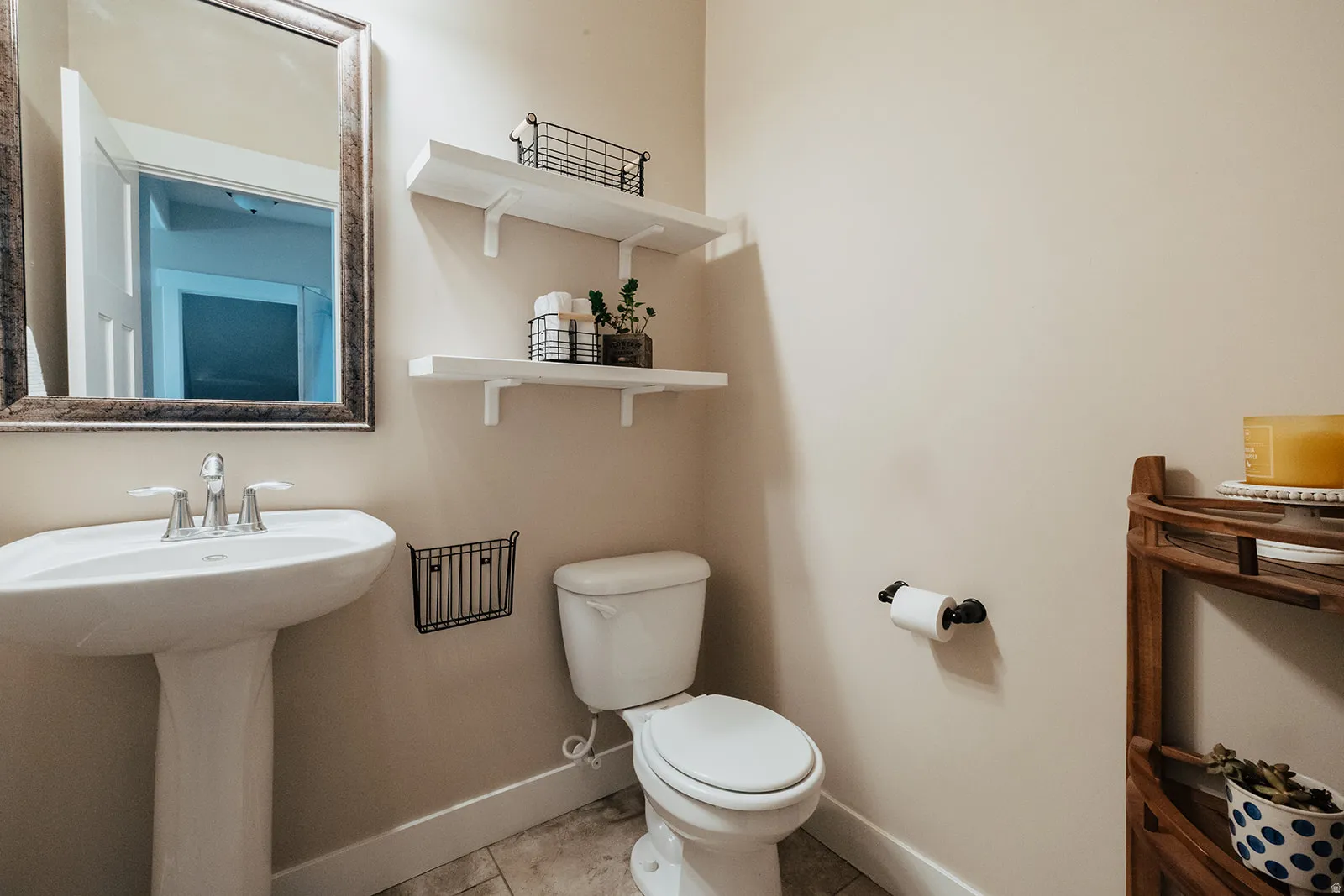 Pedestal sink with chrome faucet, framed mirror, and two wall-mounted shelves