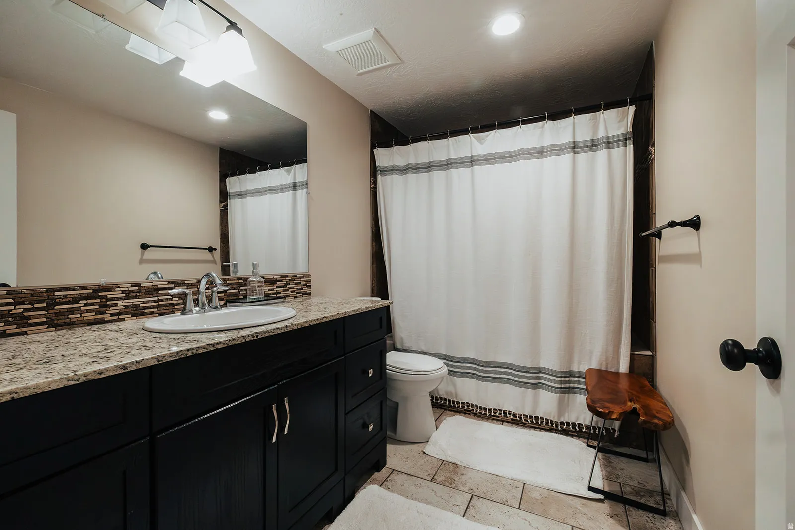 Bathroom featuring a long granite countertop vanity with a single basin, dark wood cabinetry, and a mosaic tile backsplash