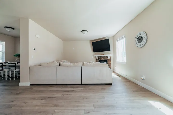 Open-concept living space featuring wood-finish flooring, a stone fireplace with a white mantel, and a bright window