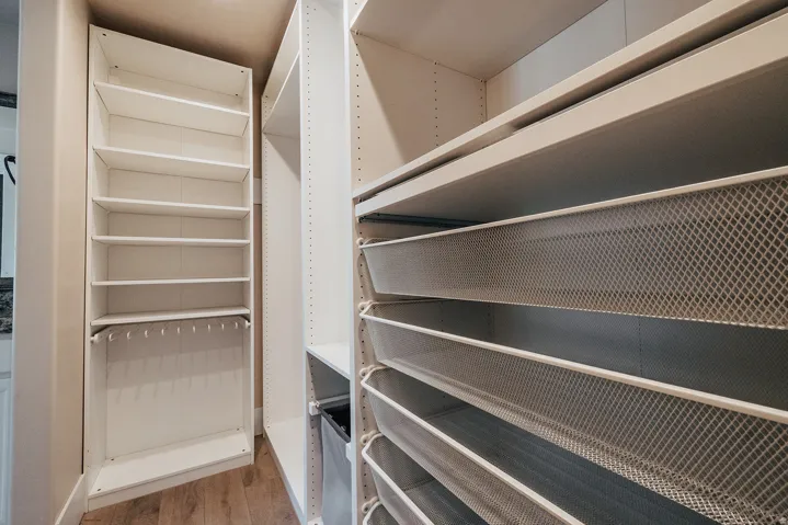 Custom closet system featuring white shelving units, multiple wire mesh pull-out drawers, and integrated hanging storage