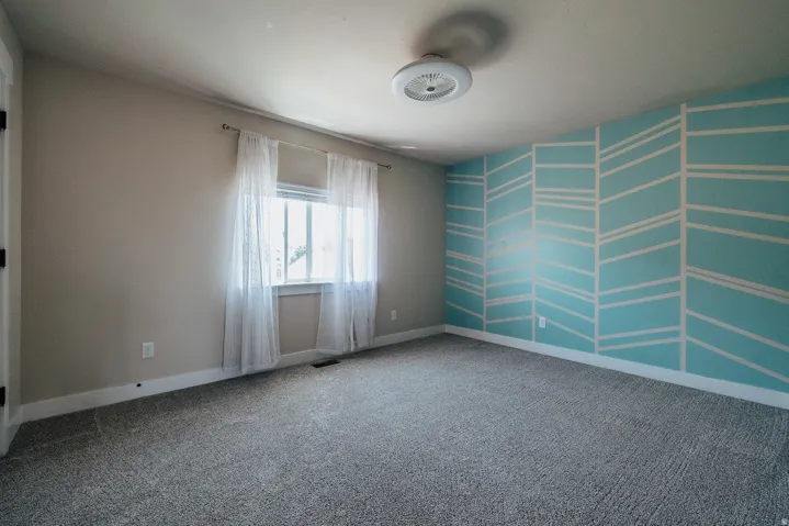 Bedroom featuring a window, patterned accent wall, neutral wall color, ceiling light fixture, and carpet flooring