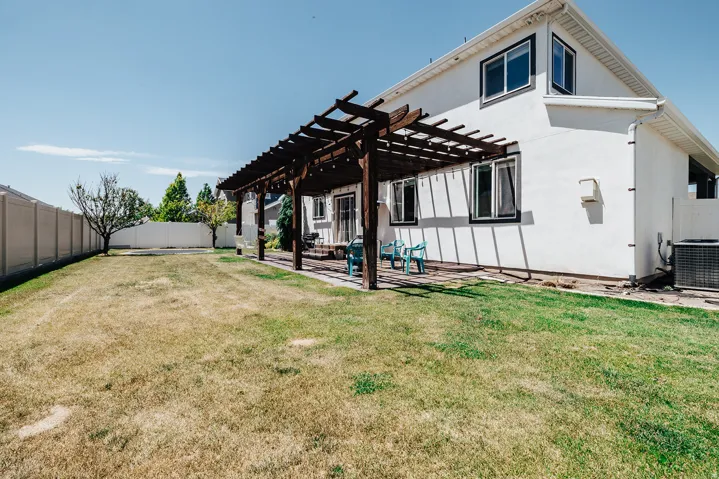 Expansive backyard featuring a pergola-covered patio, mature trees, a privacy fence, and a stucco exterior with multiple windows