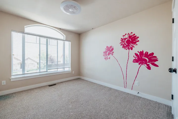 Room featuring a large window with an arched transom, beige carpeting, and a ceiling fan