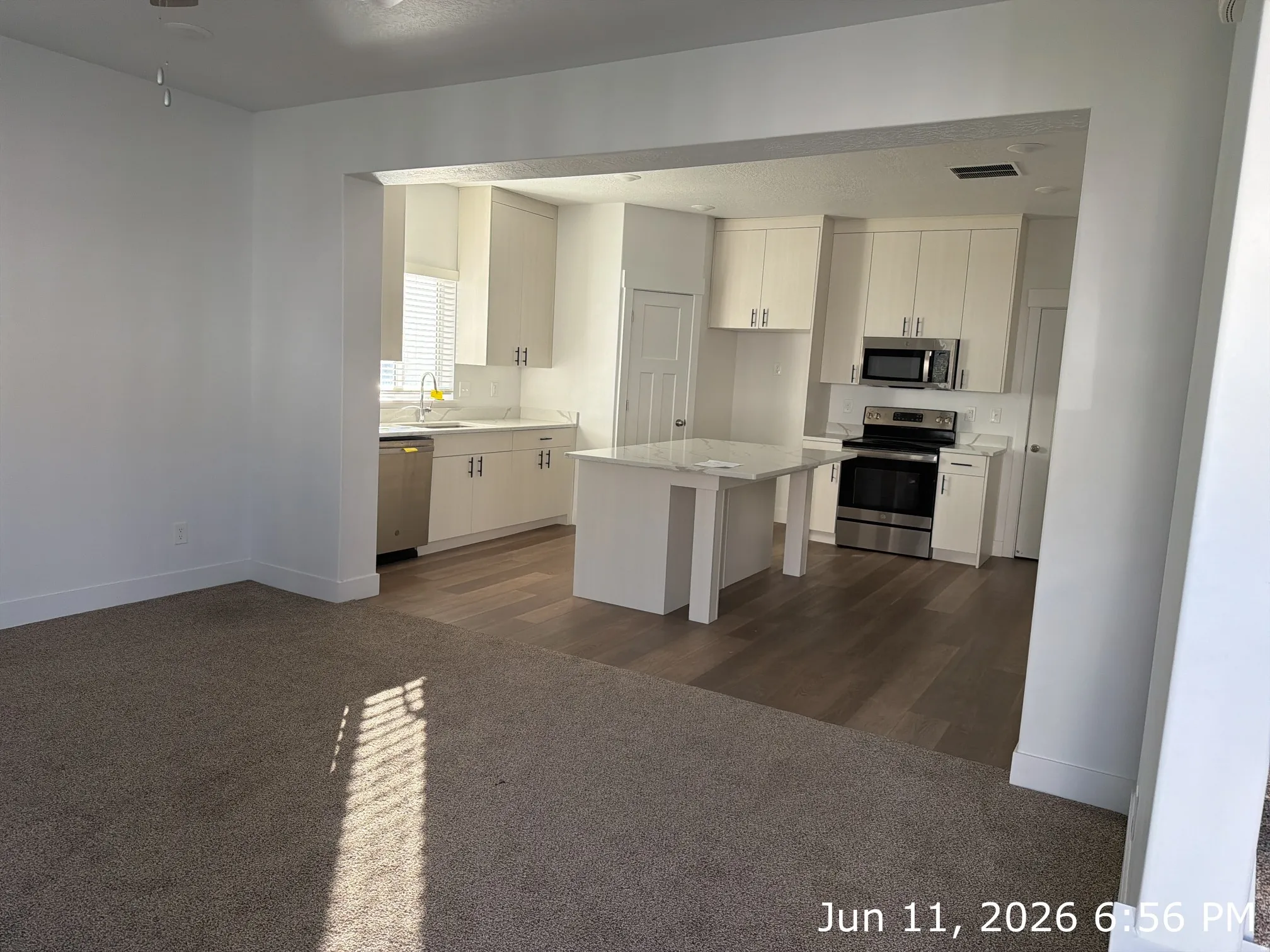 Contemporary kitchen featuring light wood-finish cabinetry, stainless steel appliances, a center island with a white countertop, and wood-finish flooring
