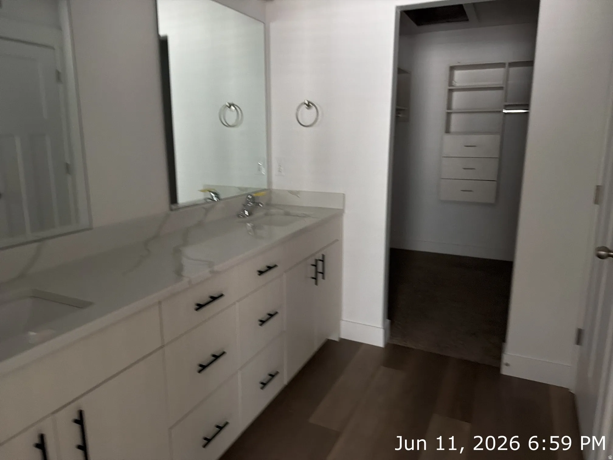 Dual-sink vanity with a white countertop and undermount sinks, accompanied by individual mirrors and dark wood-finish flooring